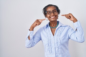 African woman with dreadlocks standing over white background wearing glasses smiling cheerful showing and pointing with fingers teeth and mouth. dental health concept.