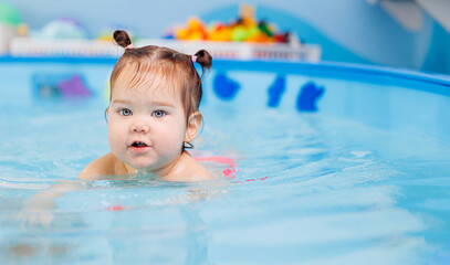 Fototapeta na wymiar Little baby swimmer. Cute happy kid girl floating in swimming pool. Sport activity for health concept