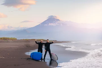 Rolgordijnen Group of friends means in wetsuit going to surf at beach. Lifestyle Extreme Surfer winter surfing in North ocean Kamchatka Russia. Friendship adventure travel sport concept © Parilov