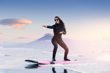 Extreme surfer woman in wetsuit with surfboard go to winter surfing in Atlantic ocean Kamchatka Russia. Adventure travel sport concept - obrazy, fototapety, plakaty