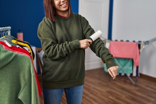 Young beautiful hispanic woman smiling confident cleaning sweatshirt using pet hair roller at laundry room