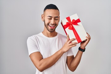Young hispanic man holding presents smiling and laughing hard out loud because funny crazy joke.
