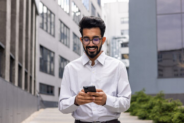 Young successful businessman walking down the street holding a phone in his hands, an Indian man...