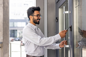 Young businessman using phone to open office door of building, man happy using wireless access,...