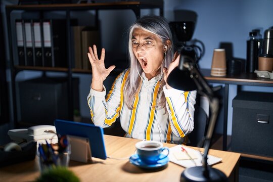 Middle Age Woman With Grey Hair Working At The Office At Night Crazy And Mad Shouting And Yelling With Aggressive Expression And Arms Raised. Frustration Concept.