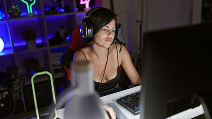 Upset young hispanic woman streamer, beautiful gamer playing video game on computer in dark gaming room, relaxing yet concentrated