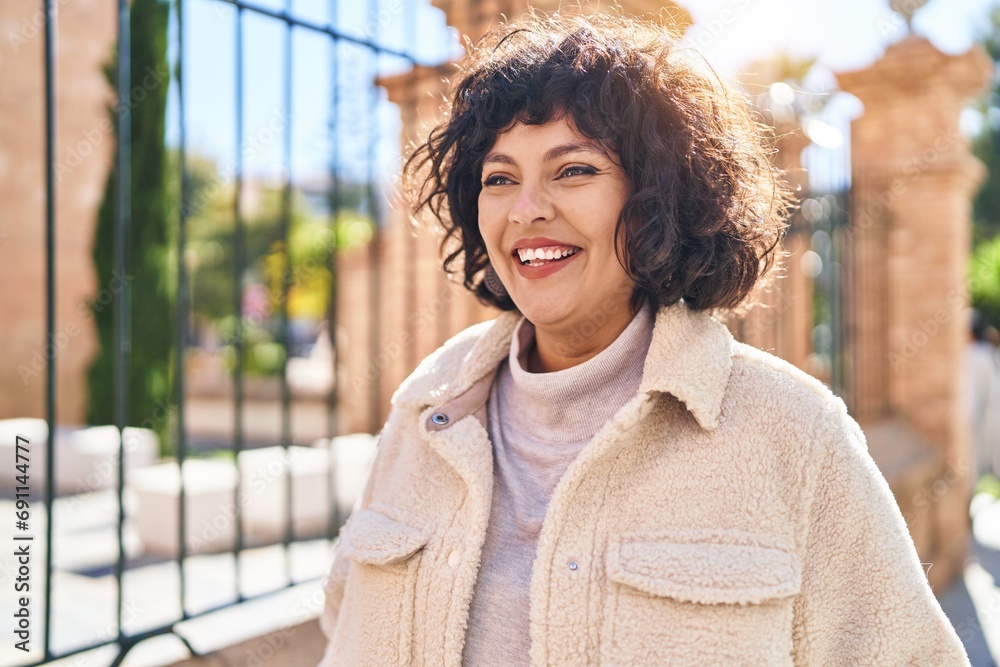 Wall mural Young beautiful hispanic woman smiling confident looking to the side at street