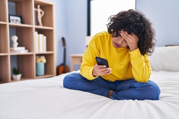 Young beautiful hispanic woman using smartphone with worried expression at bedroom