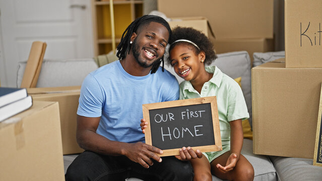 African american father and daughter holding blackboard sitting on sofa at new home