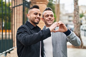 Two men couple smiling confident doing heart gesture with hands at street