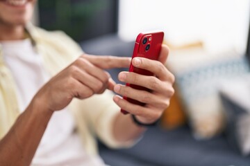 Young hispanic man using smartphone sitting on sofa at home