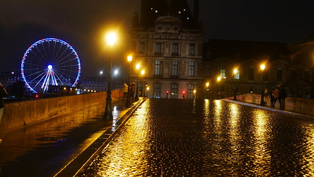 Promenade nocturne au bord de la Seine, ciel nuit noir, temps pluvieux, reflexion de lumière de lampadaires, beauté urbaine et historique, quelques marcheurs, environnement éclairé en jaune ou blanc, 