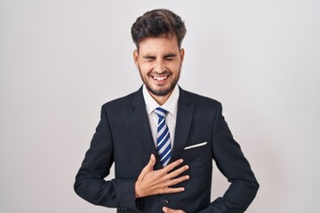 Young hispanic man with tattoos wearing business suit and tie smiling and laughing hard out loud because funny crazy joke with hands on body.