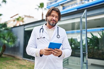 Middle age man doctor smiling confident using touchpad at hospital