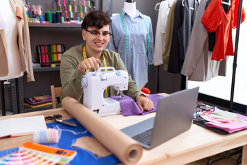 Young non binary man dressmaker designer on video call with laptop smiling happy pointing with hand and finger