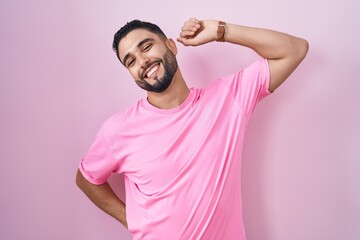 Hispanic young man standing over pink background stretching back, tired and relaxed, sleepy and...