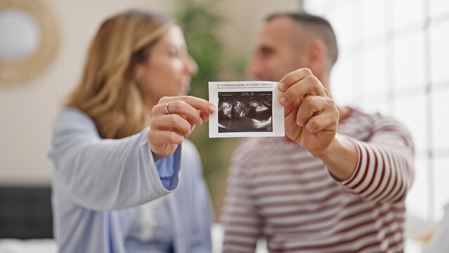 Man and woman couple holding baby ultrasound at bedroom