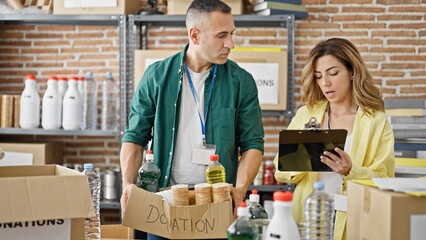 Man and woman volunteers holding package to donate writing on document at charity center