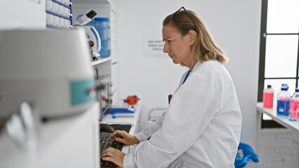 Engrossed young blonde scientist woman meticulously working on research through computer in...
