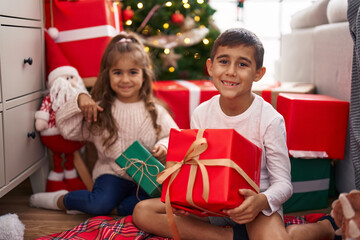 Fototapeta na wymiar Brother and sister holding gift sitting on floor by christmas gifts at home