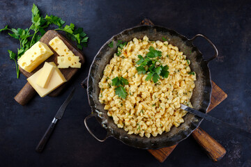 Traditional Allgäuer Käsespätzle with walnuts served as top view in a iron frying pan on a...