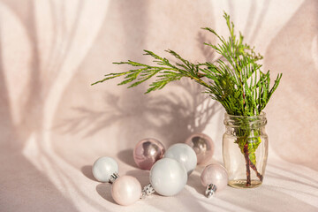 Cypress branches in transparent vases with Christmas decorations. Bouquet with evergreen spruce in natural sunlight with shadows on light pink background. Minimalist Christmas decor - obrazy, fototapety, plakaty