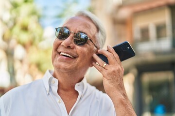 Middle age grey-haired man smiling confident listening audio message by the smartphone at street
