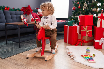 Adorable blond toddler playing with reindeer rocking by christmas tree at home