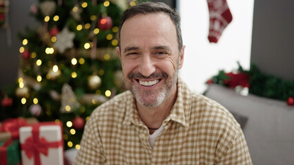 Middle age man smiling confident sitting by christmas tree at home