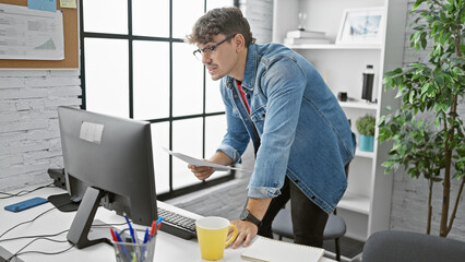 Handsome young hispanic man, an attractive boss working at the office desk, reading through important business documents while enjoying an espresso, a moment of serious concentration.