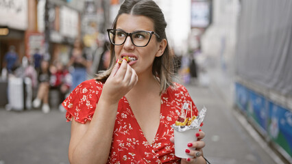 Stunning hispanic woman savors sweet potato snack in her eyeglasses on the buzzing osaka's dotonbori street