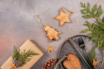 Winter holiday table setting on gray background. Dark plate, cutlery, gift box and Christmas decor. Winter holiday mood, Christmas, New Year composition. Flat lay, top view with copy space