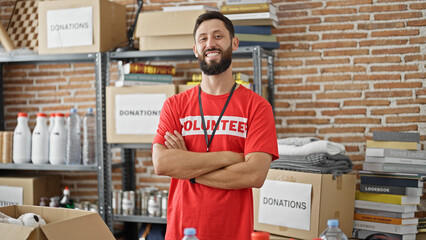 Young hispanic man volunteer standing with arms crossed gesture smiling at charity center