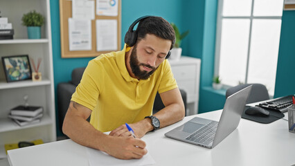 Young hispanic man business worker using laptop and headphones taking notes at the office