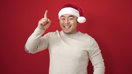Young chinese man wearing christmas hat with idea expression over isolated red background