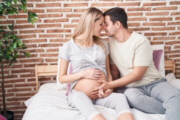 Man and woman couple touching belly sitting on bed at bedroom