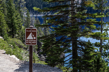 Falling Rocks No Stopping Sign in Crater Lake National Park with deep blue of lake peeking through pine trees in background.
