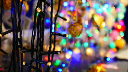 Close-up of a black wired electric garland and many others blurred behind it blinking with colorful...