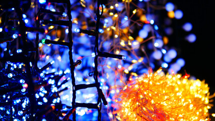 Close-up of a black wired electric garland and many others blurred behind it blinking with colorful lights