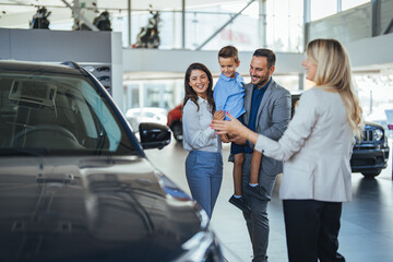 Young happy family and male salesperson using digital tablet in a car showroom. Happy young family buying their new car. Young happy family and female salesperson using digital tablet