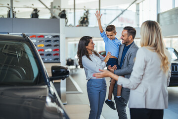 Family in a car dealership. Happy family came to an agreement with a car salesperson at a meeting in a showroom. Happy family choosing a new car in a showroom - obrazy, fototapety, plakaty