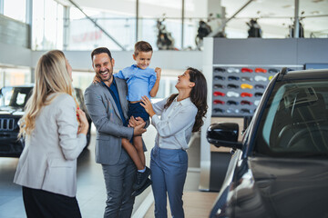Young happy family and male salesperson using digital tablet in a car showroom. Happy young family...