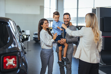 Happy family holding the keys of their new car at the dealership. Saleswoman at car dealership...