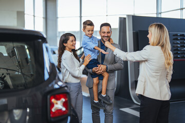Happy family choosing new car, salesman showing them luxury auto at automobile dealership store. Customers selecting vehicle, consulting manager at modern showroom shop