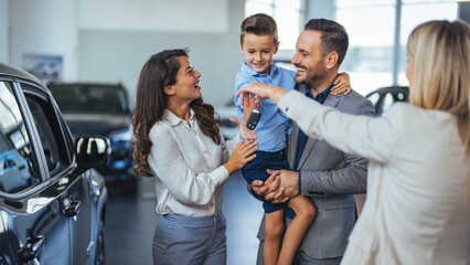 Young happy family and male salesperson using digital tablet in a car showroom. Happy young family...