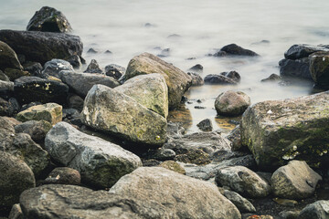 Fototapeta na wymiar Cobblestones and rocks along the seacoast with smooth water through long exposure shot