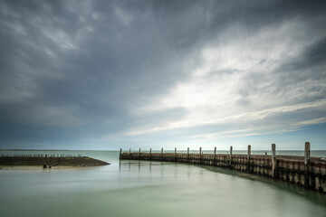 Obraz premium Urbex harbor in a round shape of weathered concrete with rusted boolders and rotten mooring posts and above a threatening cloudy sky