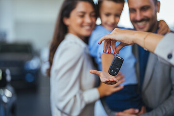 Happy family holding the keys of their new car at the dealership. Saleswoman at car dealership...