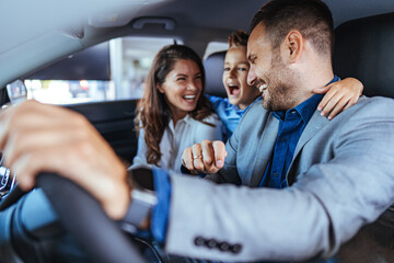 Happy family choosing new car, salesman showing them luxury auto at automobile dealership store....