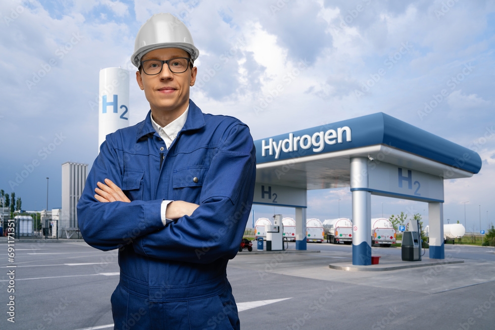 Poster engineer in a helmet and blue suit on a background of hydrogen filling station using renewable energ